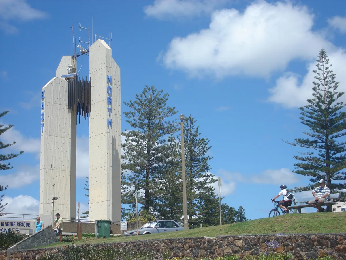 Point Danger Lighthouse above a green headland lawn, with Norfolk Island pines and visitors nearby