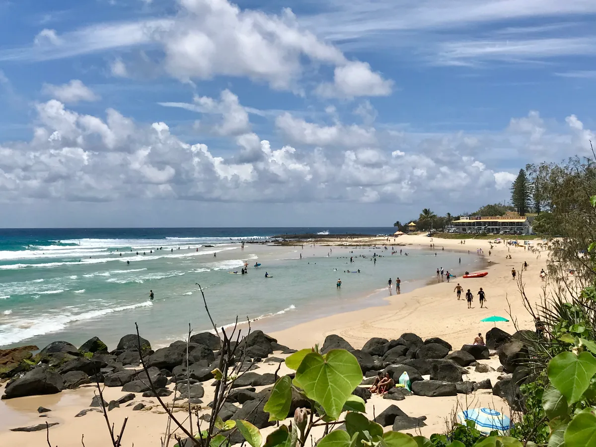 Rainbow Bay beach seen from Greenmount Hill, with surfers in the water and the surf club beyond