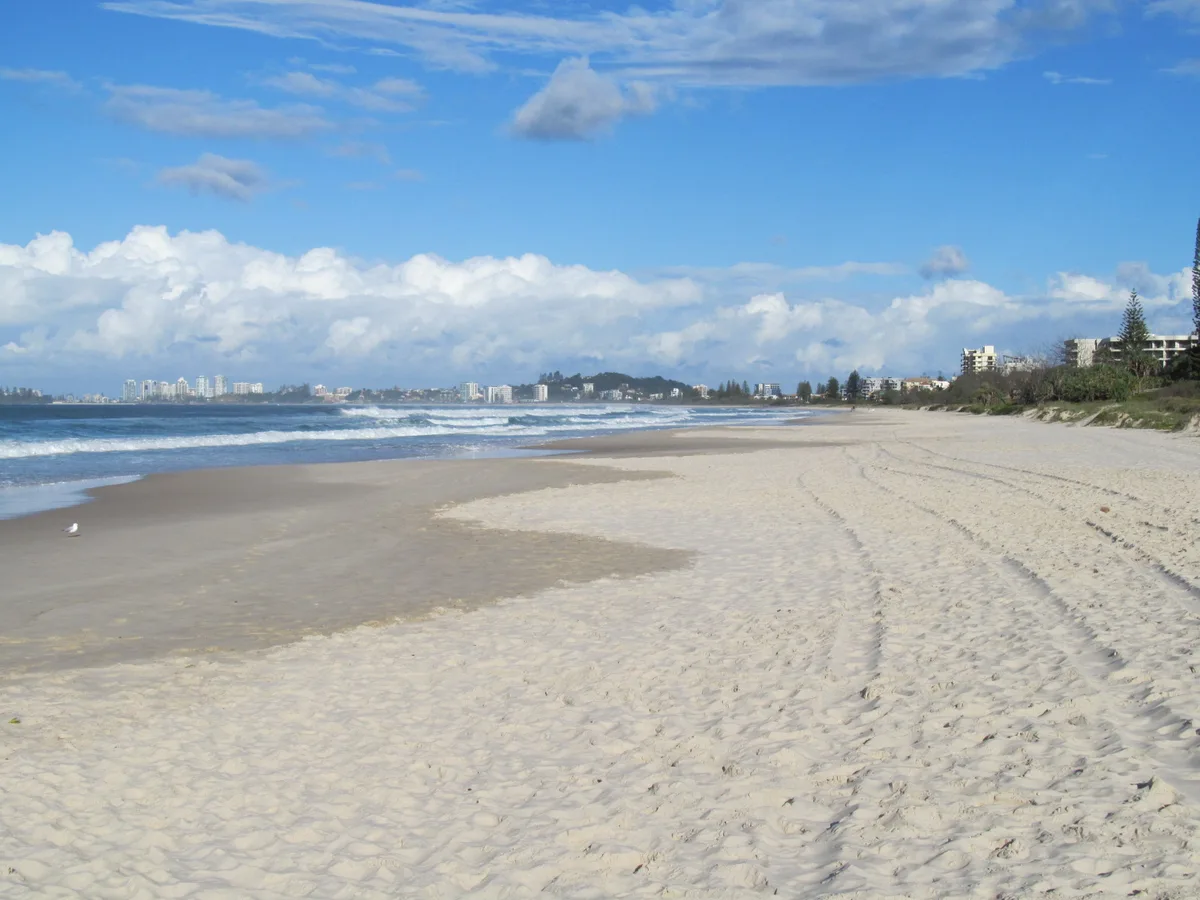 Waves along Tugun Beach, with coastal buildings and a headland in the distance